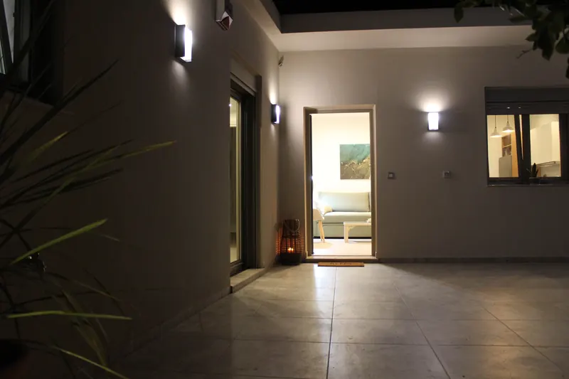 The terrace at night: wall lamps lit on the facade, the front door open onto the lit living room