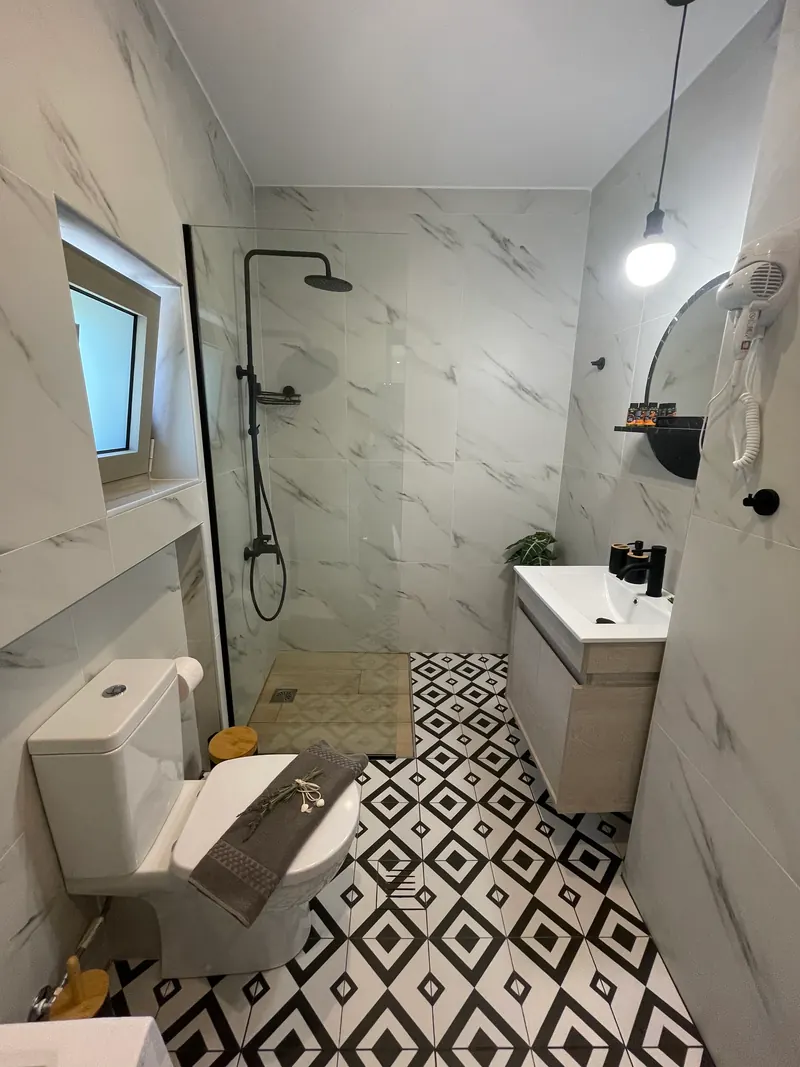The bathroom: walk-in shower with black fittings, marble-effect walls and a black-and-white patterned floor