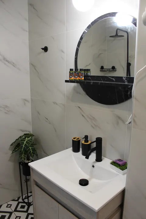 The bathroom washbasin with black tap and a round mirror