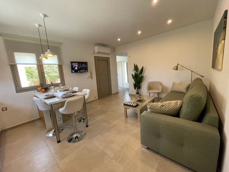 Open-plan living room with a sage-green sofa, a high table with white chairs and the kitchen beyond