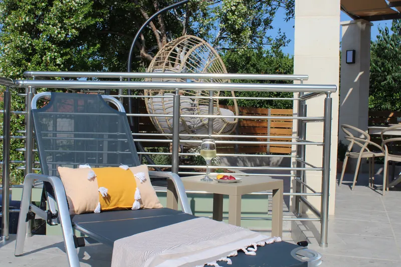 A sun lounger with a yellow cushion on the deck, a hanging egg chair behind it among the trees