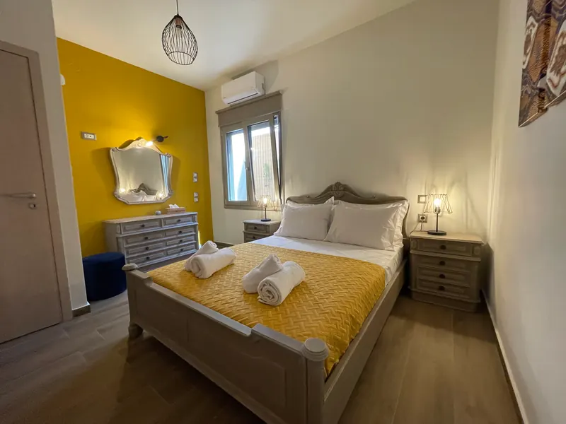 The Mustard Room: a carved grey-washed bed with a yellow quilt, a dresser and mirror against a mustard-yellow wall