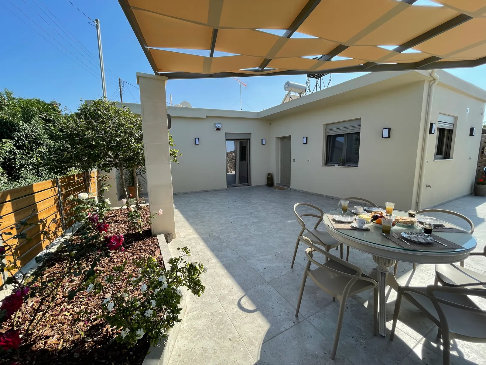 The terrace of Aryiro's Residence under shade sails, with a round table laid for breakfast and the house behind