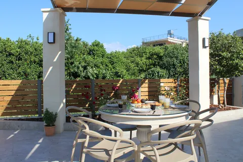 The round breakfast table under the pergola, wooden fence behind